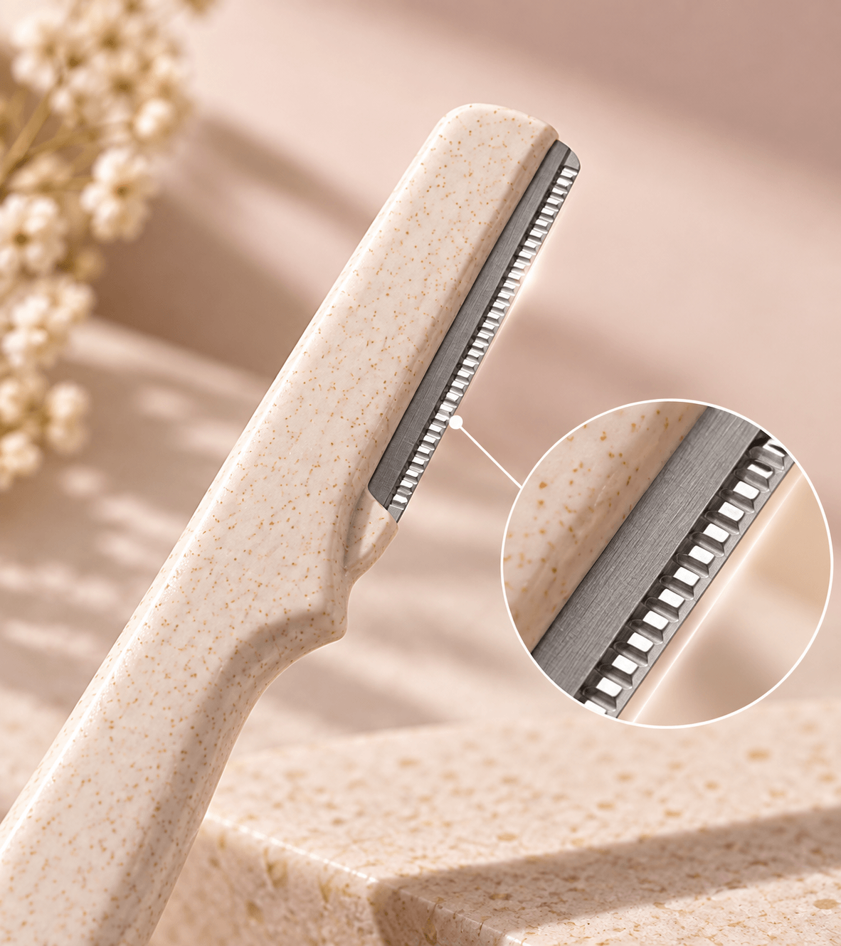 Close-up of a beige spa-style facial razor with a circular inset showing the metal blade edge, set against a warm beige background with dried flowers.